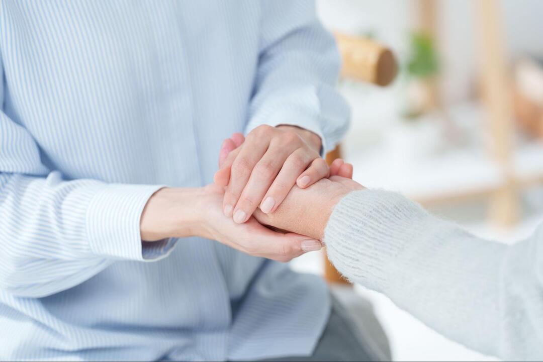 患者と思われる人の手を両手で優しく包み込むように握っている手元のアップ