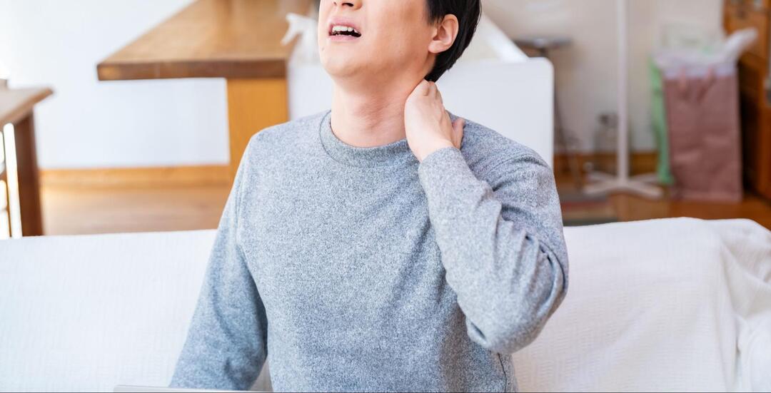男性が、苦悶の表情を浮かべながら左手で首の後ろ（うなじ辺り）を押さえている様子