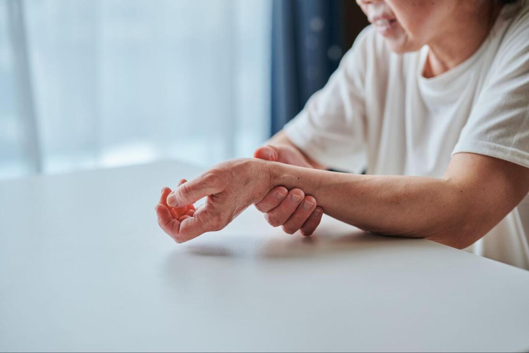高齢の人物が、しびれや痛みを表すように右手で左の手首辺りをつかんでいる手元のアップ