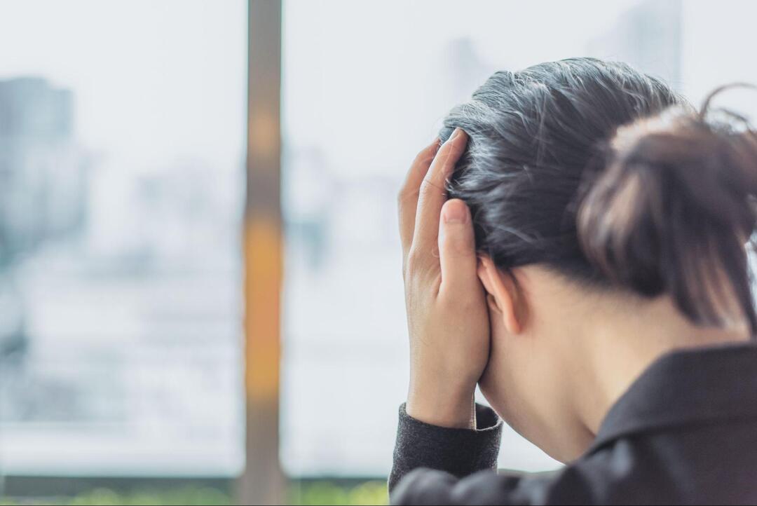 両手で頭を抱え込み、苦悩や痛みに耐えるようにうつむいている女性の後ろ姿