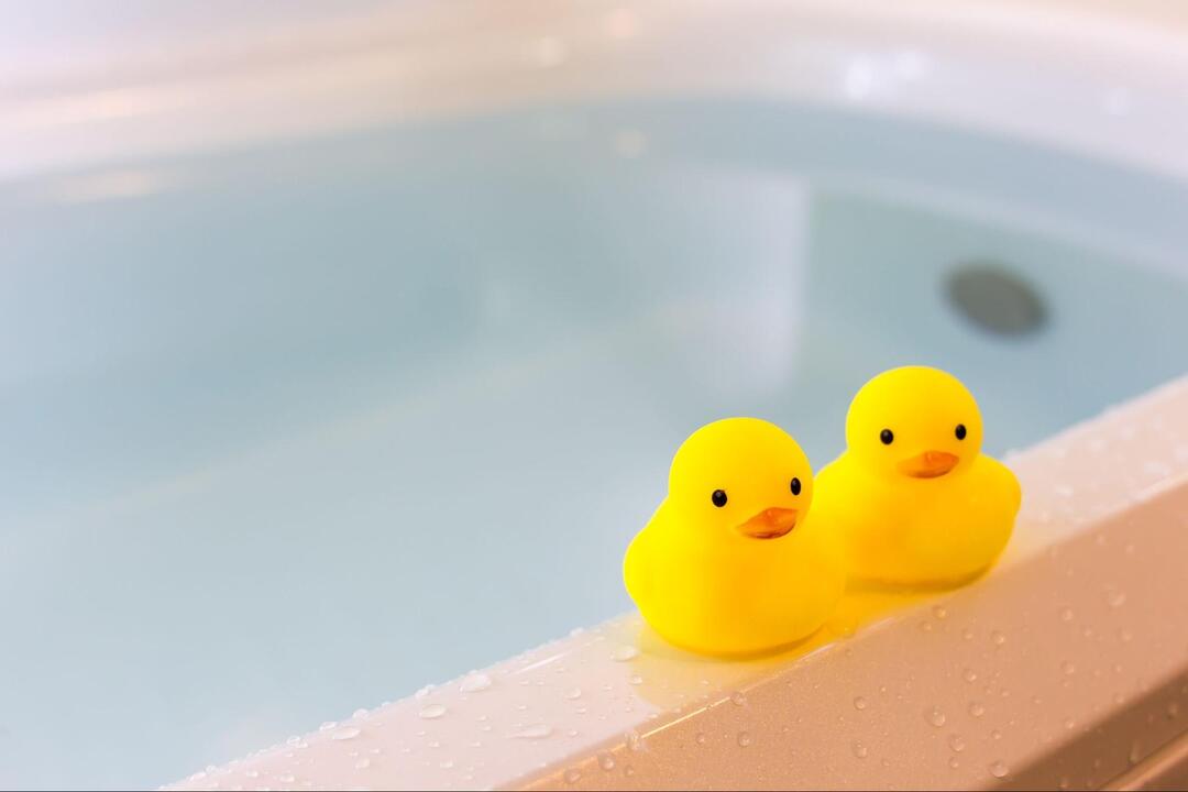 水が張られたお風呂の浴槽の縁に、2匹並んで置かれている黄色いゴム製のアヒルの玩具