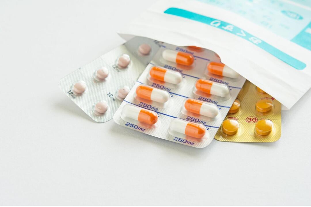 「おくすり」と書かれた調剤薬局の袋の上に重ねられた、オレンジと白のカプセル剤や丸い錠剤の複数のPTPシート