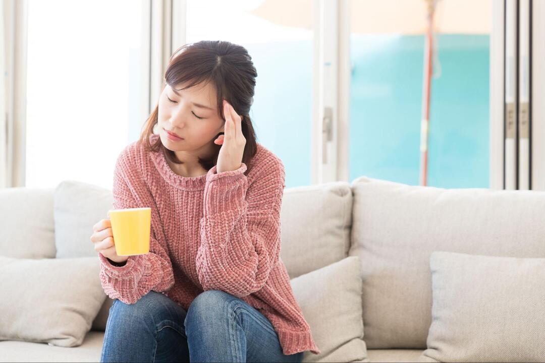 女性が目を閉じて左手でこめかみを押さえて頭痛に耐えている様子
