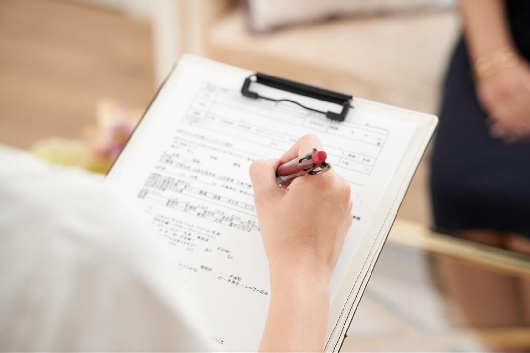 バインダーに挟まれた問診票のような書類に、ボールペンで記入している手元のアップ