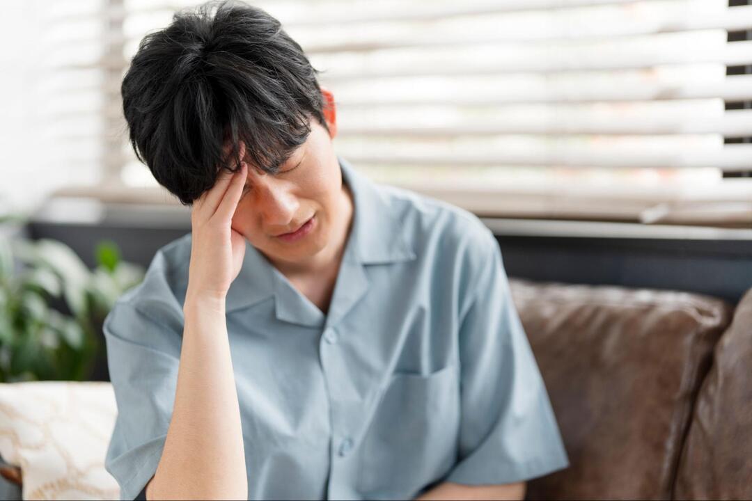 男性が目を閉じ、右手で額を押さえながら頭痛に耐えている様子