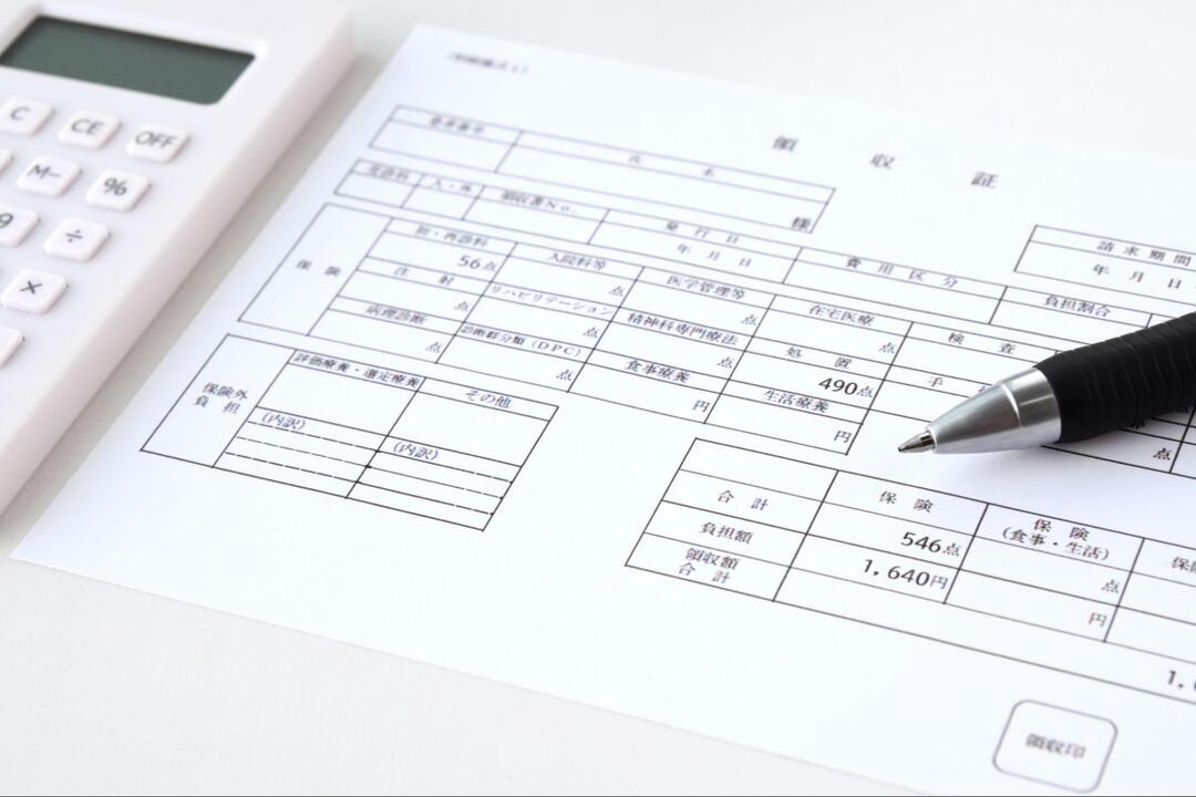 電卓とボールペンが添えられた、診療費や負担額が記載されている医療費領収書・明細書