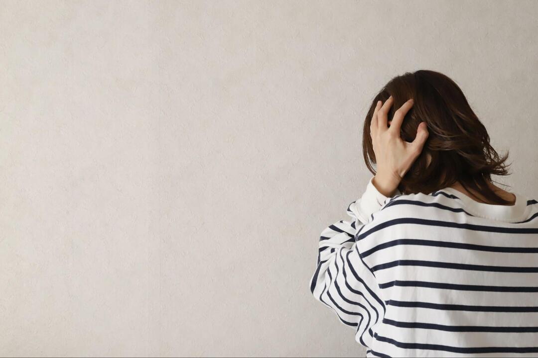 後ろ向きの人物が、頭痛や不調を訴えるように頭の後ろへ手を当てている様子