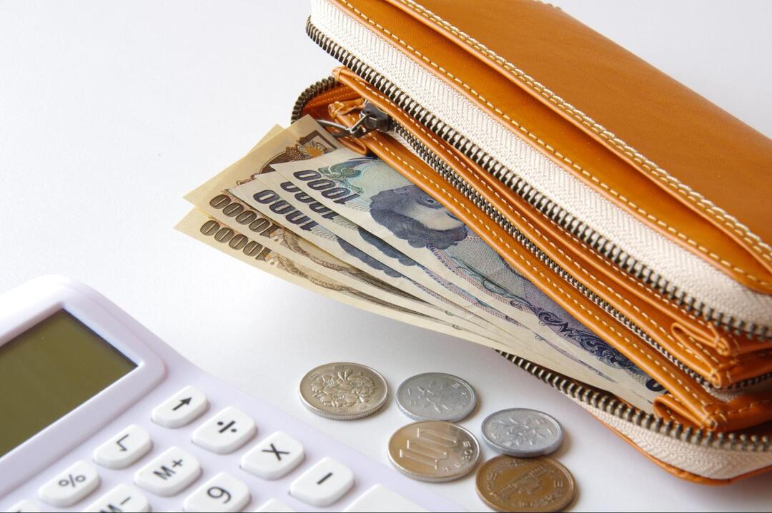 長財布から覗く日本円の紙幣と手前に散らばる硬貨、そして白い電卓の一部